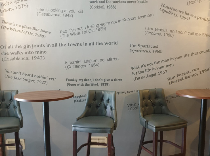 Wall of iconic quotes from films with tables and chairs in front.